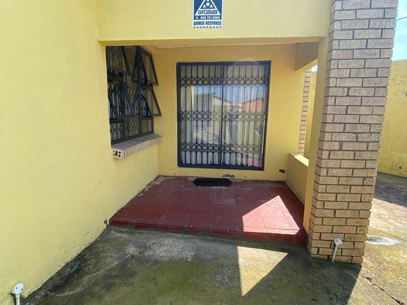 A covered patio area featuring tiled flooring, a brick support pillar, and security gate access to the interior.