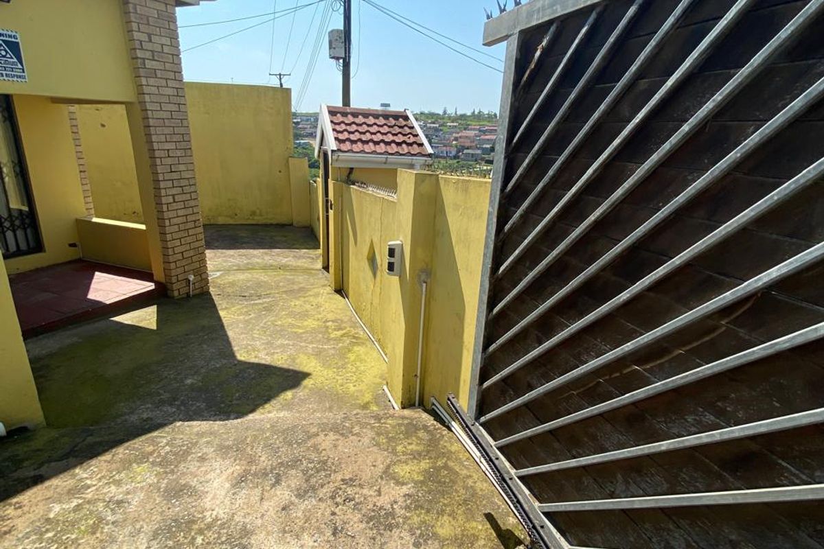 Rear exterior area featuring a sliding gate with security spikes, a boundary wall, and a concrete patio surface requiring maintenance.