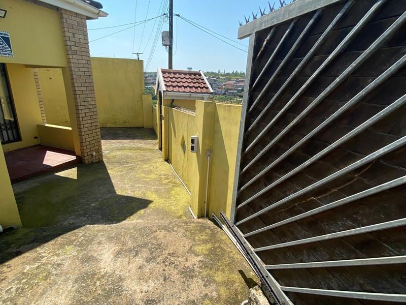 Rear exterior area featuring a sliding gate with security spikes, a boundary wall, and a concrete patio surface requiring maintenance.