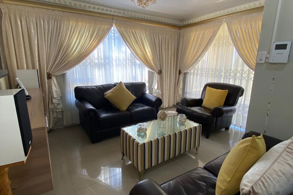 A living room featuring tiled flooring, decorative ceiling cornices, and large windows fitted with security gates.