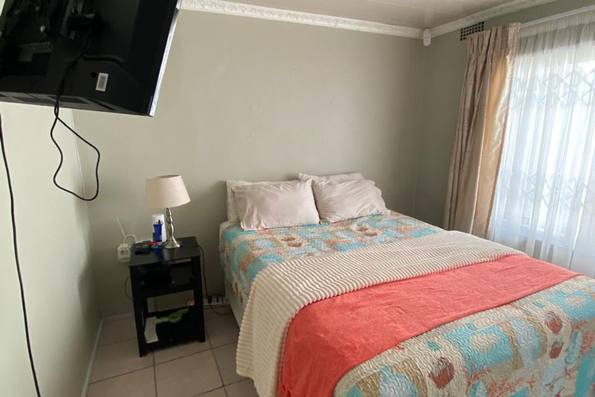 A functional bedroom featuring tiled flooring, ceiling cornice detailing, and a window fitted with security gates and curtains.