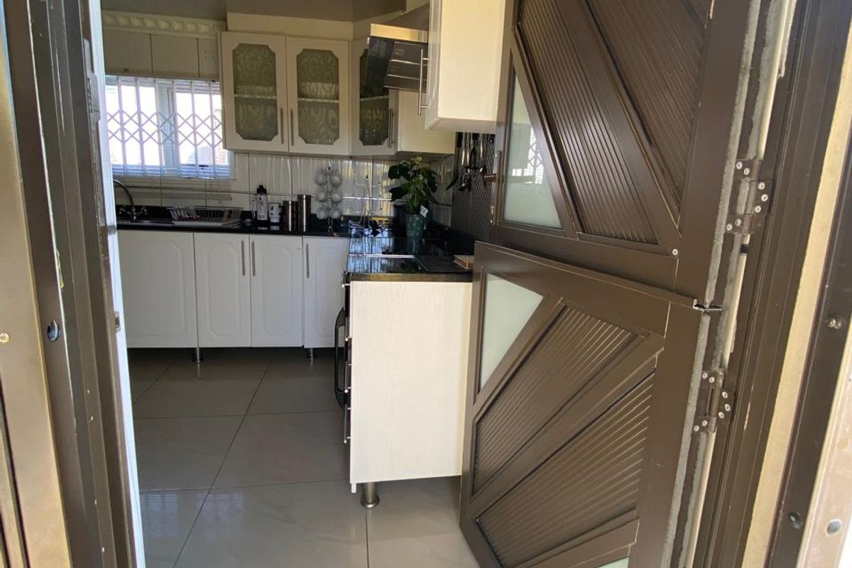 A functional kitchen featuring white cabinetry, dark countertops, and tiled flooring, accessed through a secure metal door.