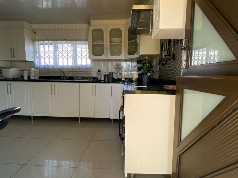 A functional kitchen featuring white cabinetry, tiled flooring, a built-in extractor fan, and security bars on the window.