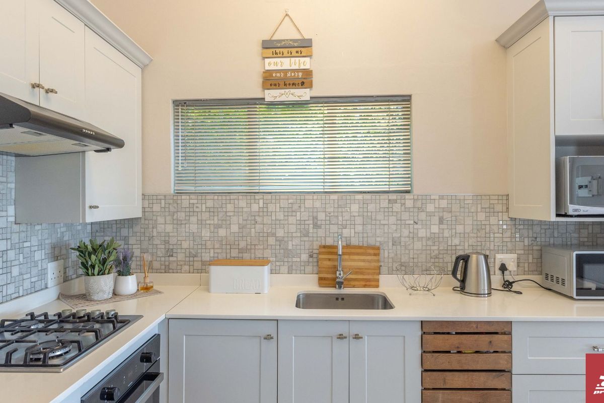 A well-maintained kitchen featuring shaker-style cabinetry, stone countertops, a mosaic tile backsplash, and integrated appliances including a gas hob and oven.