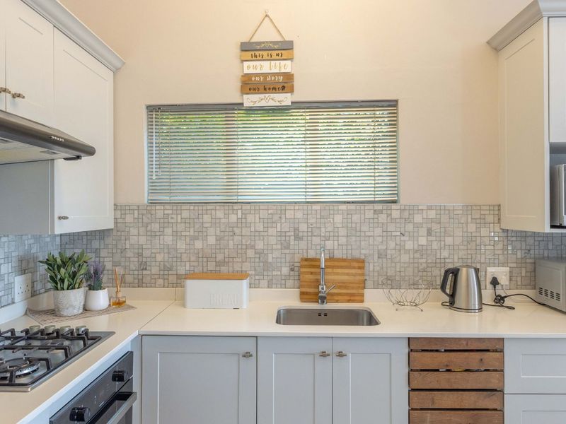 A well-maintained kitchen featuring shaker-style cabinetry, stone countertops, a mosaic tile backsplash, and integrated appliances including a gas hob and oven.
