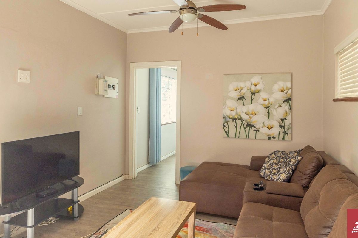 A living room featuring laminate flooring, a ceiling fan, and an exposed electrical distribution board, providing a functional and neutral living space.
