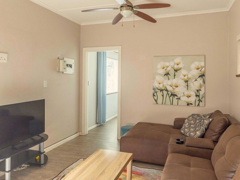 A living room featuring laminate flooring, a ceiling fan, and an exposed electrical distribution board, providing a functional and neutral living space.
