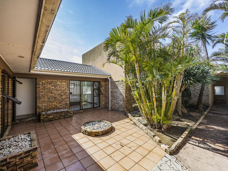 A private outdoor patio area featuring tiled flooring, built-in brick planters, and direct access to the home through security-gated entrances.