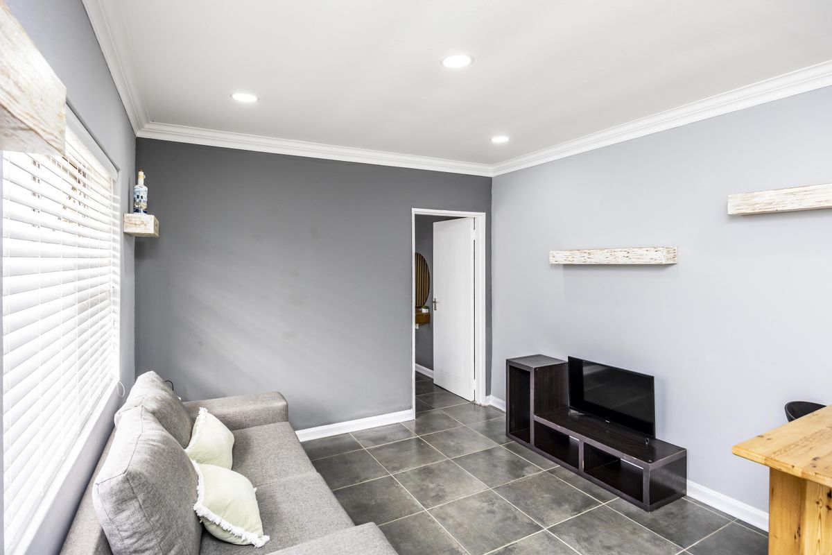 A well-lit living room featuring neutral grey walls, crown molding, recessed downlights, and dark tiled flooring.