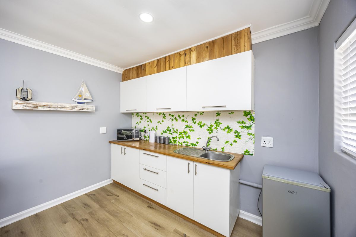 A compact kitchen area featuring white cabinetry, a wooden countertop, stainless steel sink, and a decorative backsplash with wood-paneled upper accents.