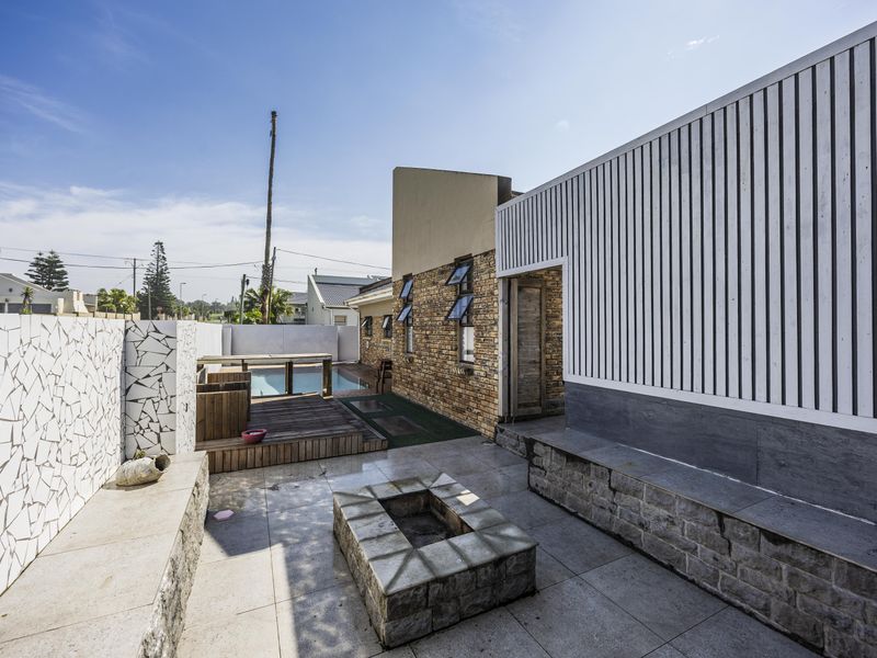 Outdoor patio area featuring a built-in fire pit, timber decking, stone-clad walls, and access to a swimming pool.