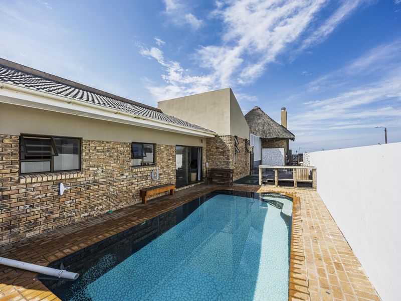 Outdoor pool area featuring a swimming pool with brick surround, set against a brick-clad house exterior with a tiled roof.