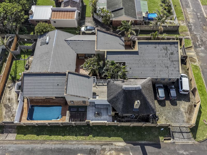 Aerial view of the property showcasing the main residence with a combination of tiled and thatched roofing, swimming pool, and paved driveway.