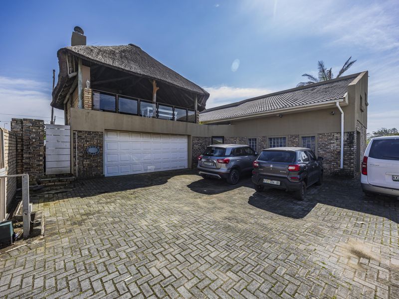 Front exterior view of the property featuring a double garage, paved driveway, and a distinctive thatched roof upper balcony area.