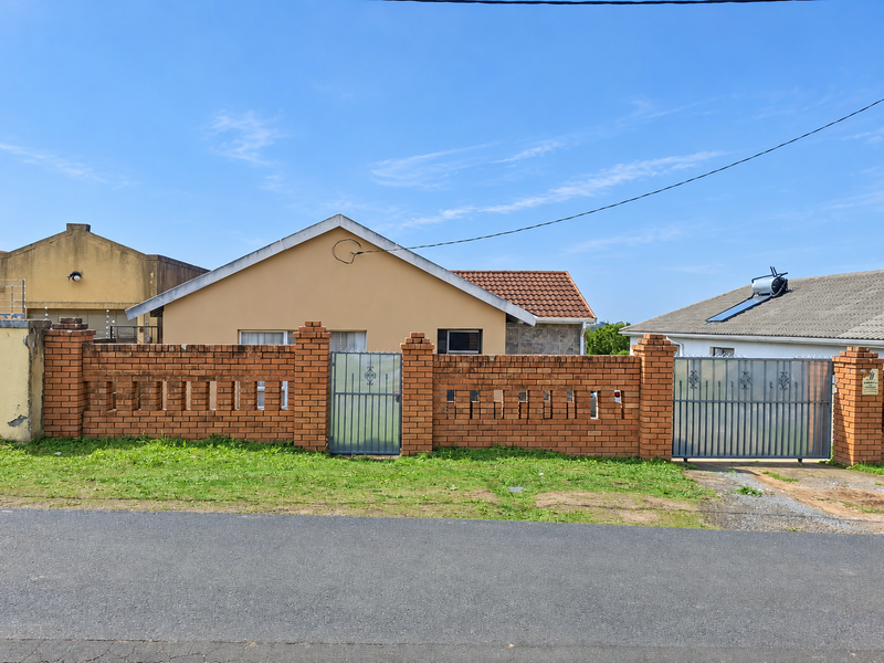 Front view of a single-story house featuring a brick boundary wall, metal gates, and a tiled roof with a solar water heating system.