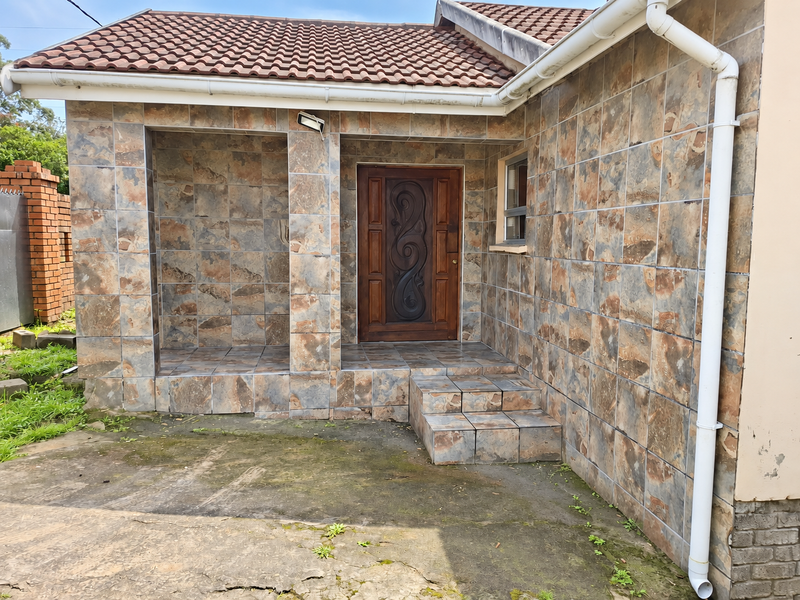 Front entrance area featuring decorative tiled facade, tiled steps, and a solid wooden front door with integrated guttering and downpipe system.