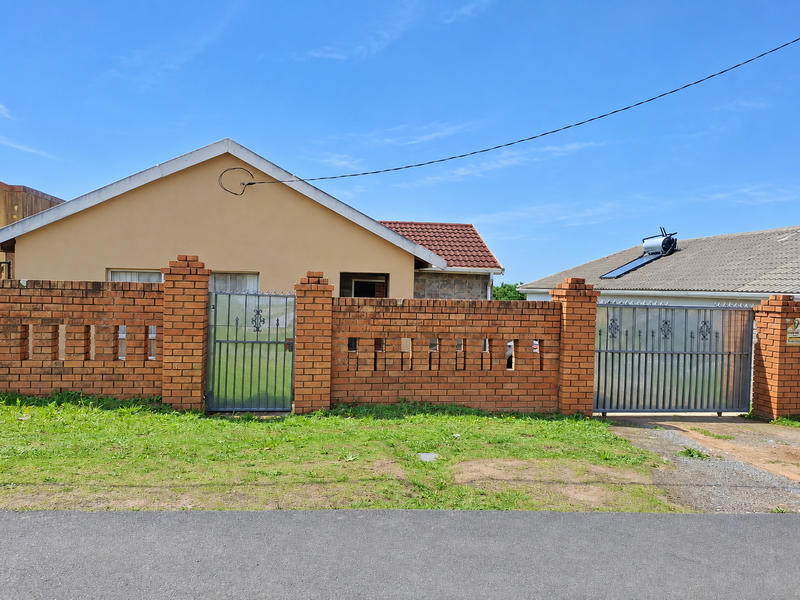 Front view of a single-story house featuring a brick boundary wall, metal gates, and a solar water heating system on the roof.