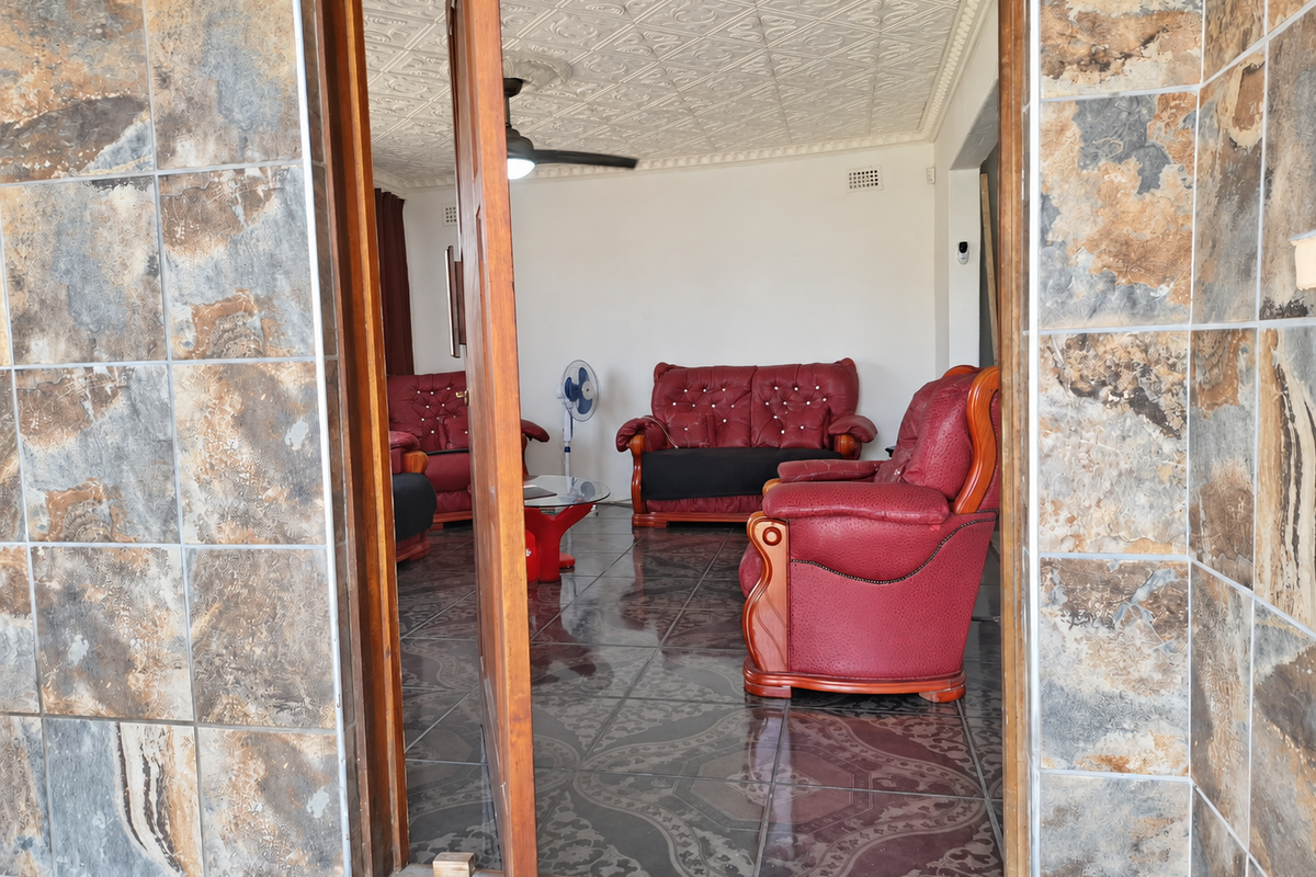 A living room viewed through a doorway, featuring decorative ceiling tiles, a ceiling fan, and dark patterned floor tiles.