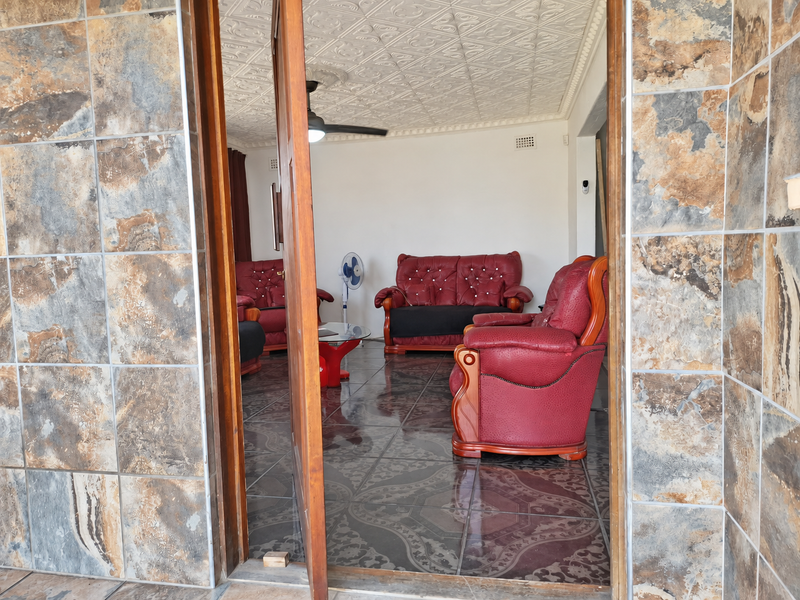 A living room viewed through a doorway, featuring decorative ceiling tiles, a ceiling fan, and dark patterned floor tiles.