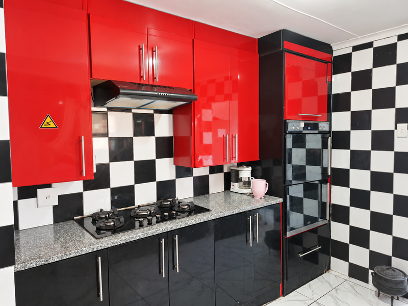 A modern kitchen featuring high-gloss red and black cabinetry, granite countertops, a gas hob, extractor fan, and a built-in double oven with checkerboard tiling.