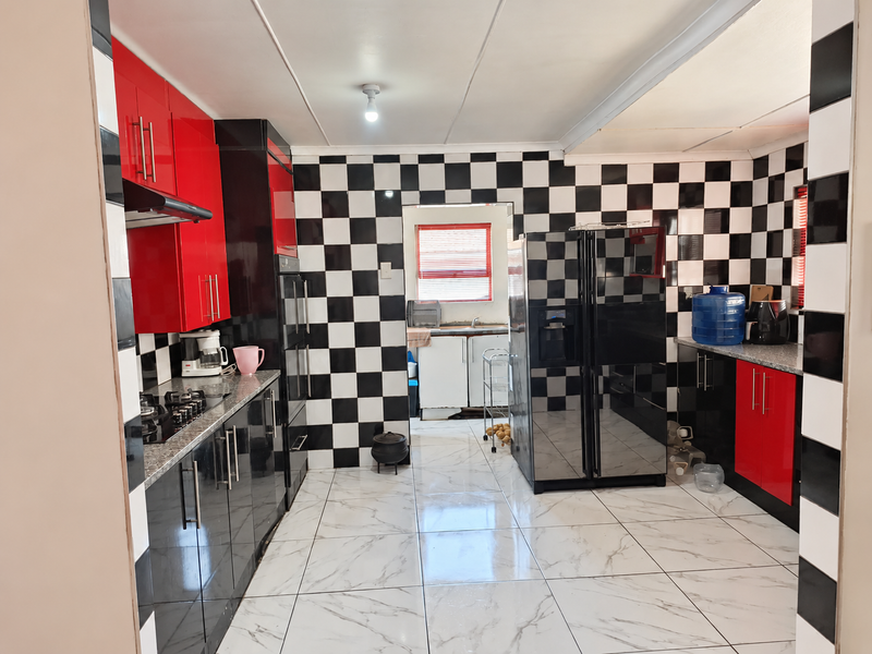 A kitchen featuring high-gloss red and black cabinetry, granite countertops, a gas hob, and a distinctive black and white checkered wall tile design.