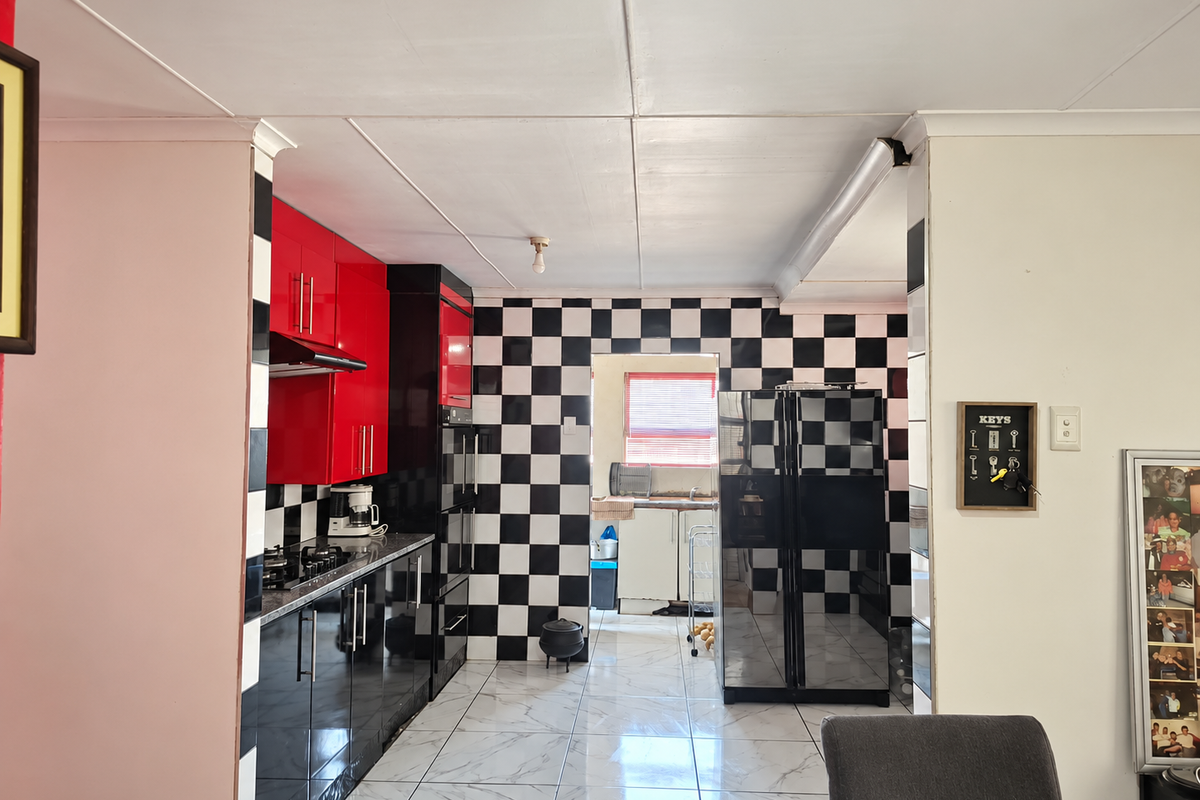 A kitchen featuring high-contrast red and black cabinetry, a checkerboard tiled backsplash, and marble-look floor tiles, leading through to a secondary scullery area.