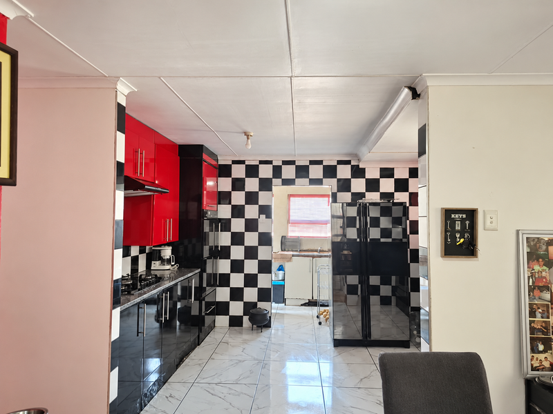 A kitchen featuring high-contrast red and black cabinetry, a checkerboard tiled backsplash, and marble-look floor tiles, leading through to a secondary scullery area.