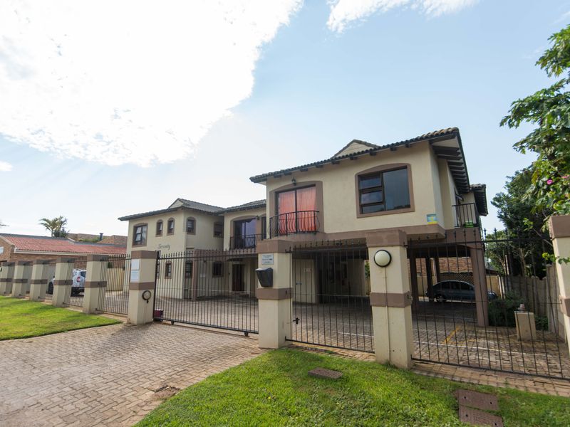 Front elevation of a multi-unit townhouse complex featuring a paved driveway, secure metal gate, and balcony access.