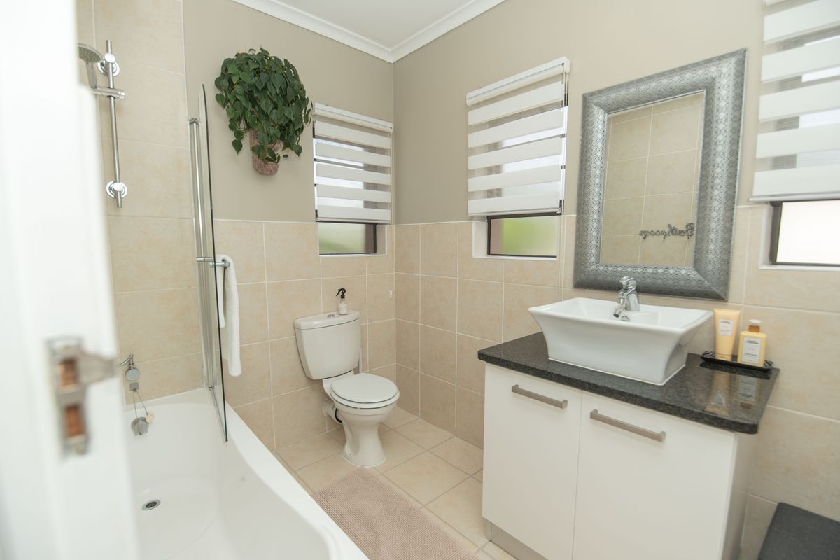 A well-maintained bathroom featuring a bathtub with a glass shower screen, a modern vessel sink vanity, and neutral wall and floor tiling.