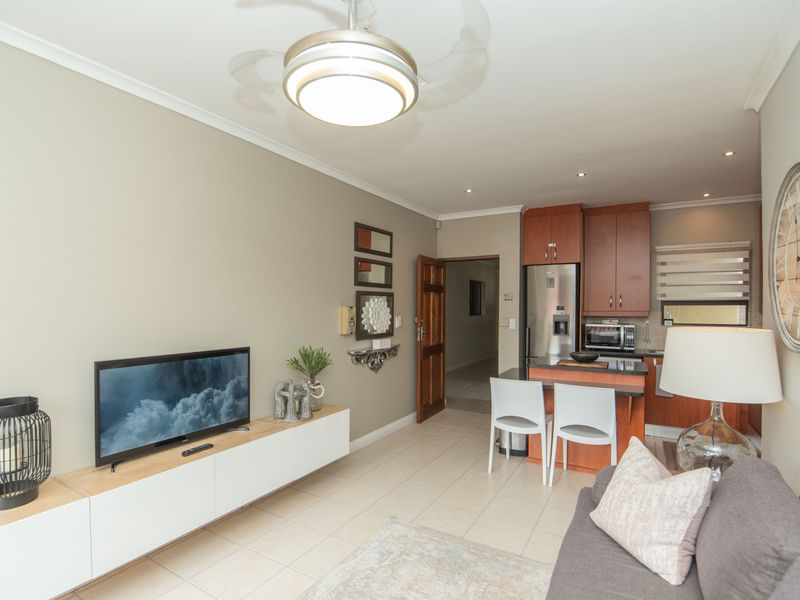 Open-plan living area featuring tiled flooring, a modern kitchen with granite countertops, and a ceiling fan, creating a functional and cohesive space.