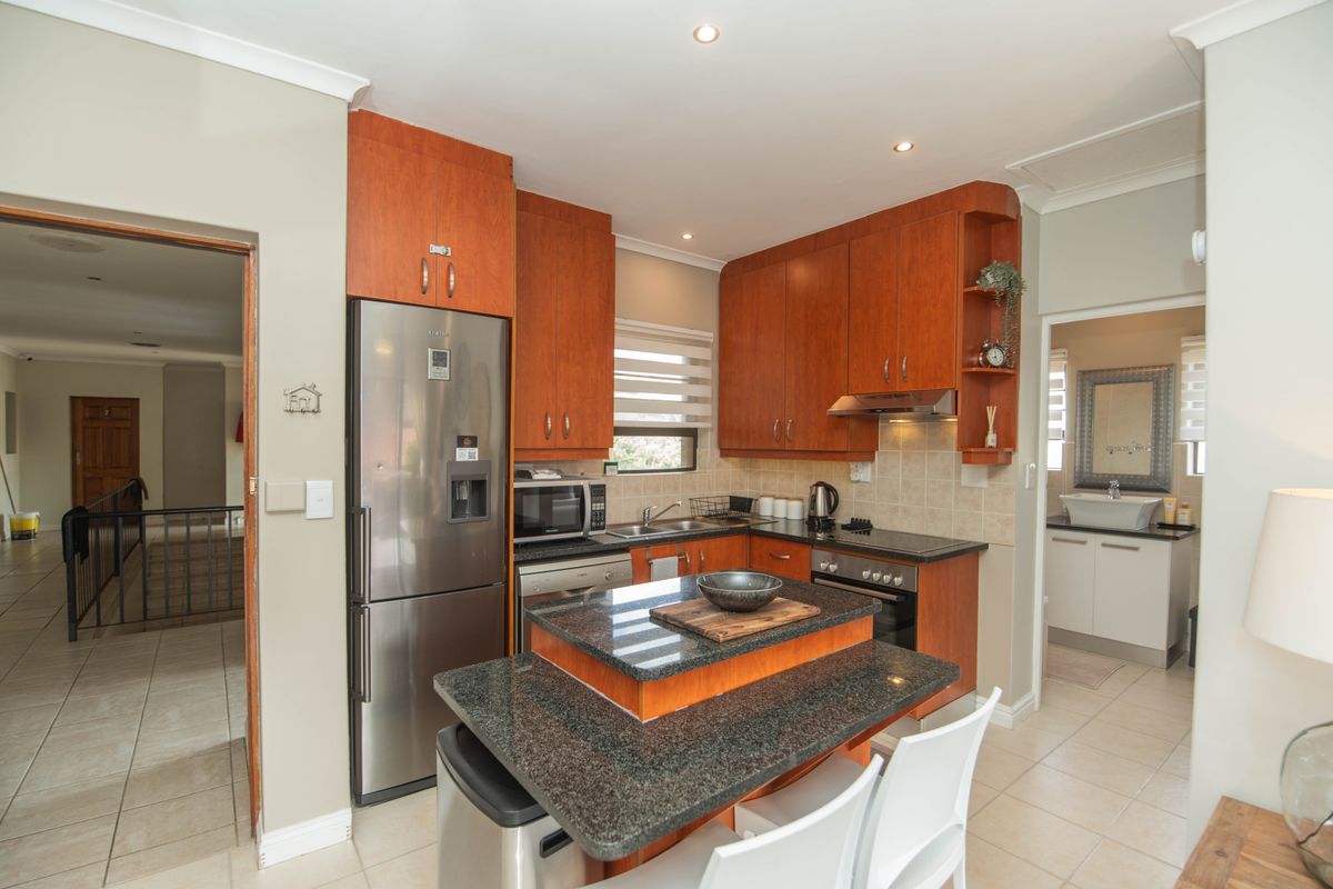 A functional kitchen featuring warm-toned wooden cabinetry, granite countertops, a central island, and integrated stainless steel appliances with tiled flooring.