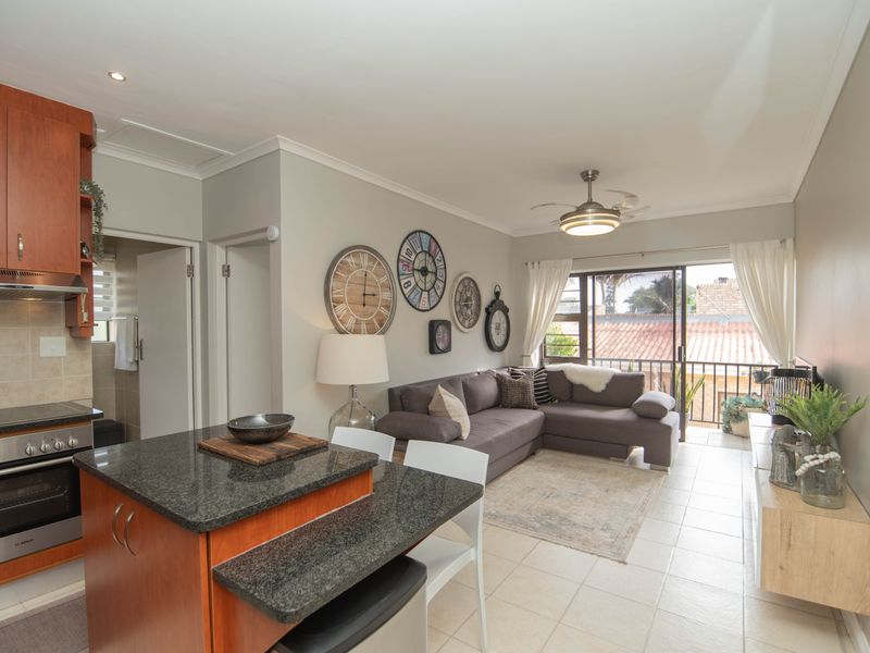 Open-plan living area featuring a kitchen with granite countertops, built-in oven, and tiled flooring, leading to a balcony through sliding glass doors.