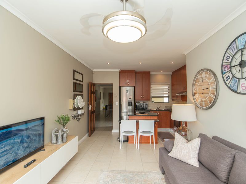 Open-plan living area featuring tiled flooring, a compact kitchen with built-in cabinetry, and a breakfast island, creating a functional and connected living space.