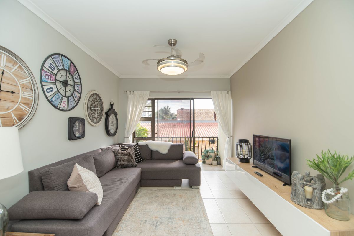 A well-maintained living room featuring tiled flooring, a ceiling fan, and sliding glass doors that open onto a balcony.