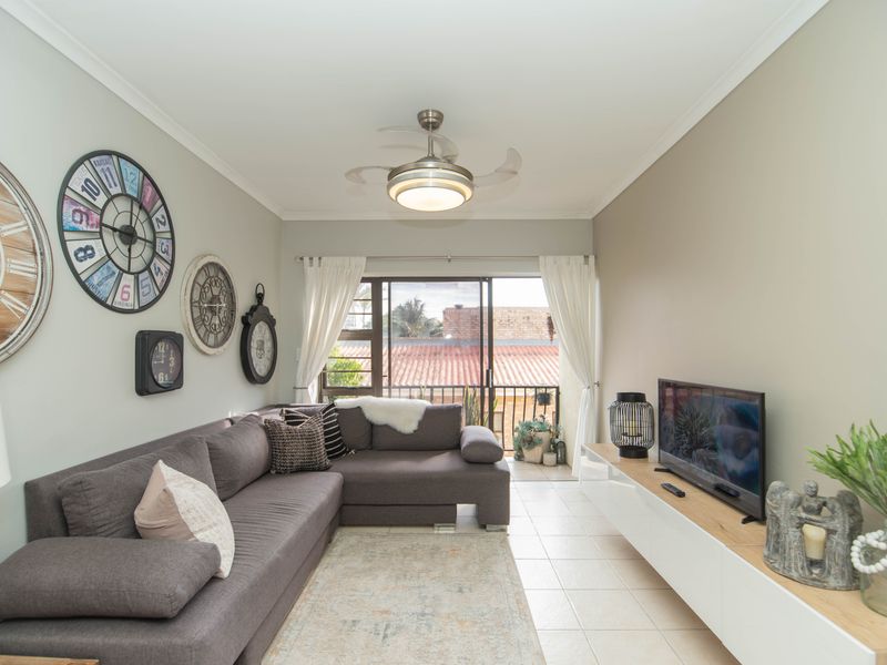 A well-maintained living room featuring tiled flooring, a ceiling fan, and sliding glass doors that open onto a balcony.