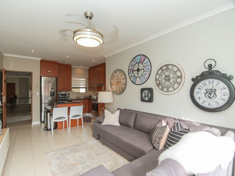 Open-plan living area featuring tiled floors, a modern ceiling fan, and a compact kitchen with built-in cabinetry and stainless steel appliances.