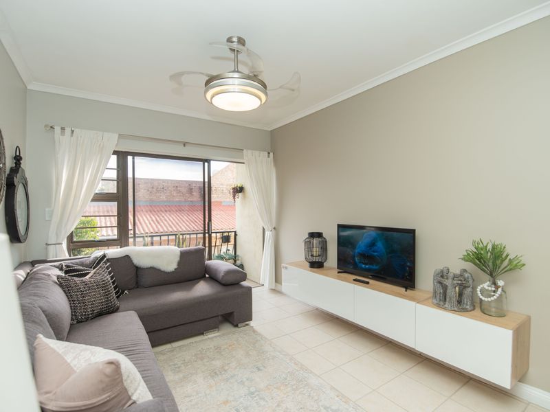 A well-maintained living room featuring tiled flooring, a modern ceiling fan, and a sliding glass door providing access to an outdoor balcony area.