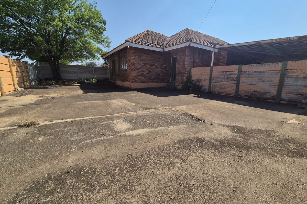 Rear exterior view of a brick house featuring a large concrete driveway, a carport, and perimeter precast concrete walling.