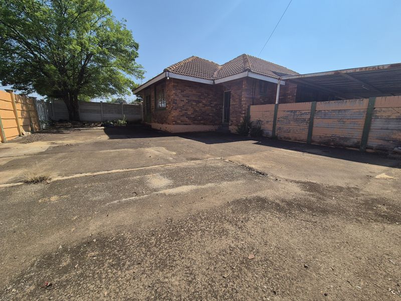 Rear exterior view of a brick house featuring a large concrete driveway, a carport, and perimeter precast concrete walling.