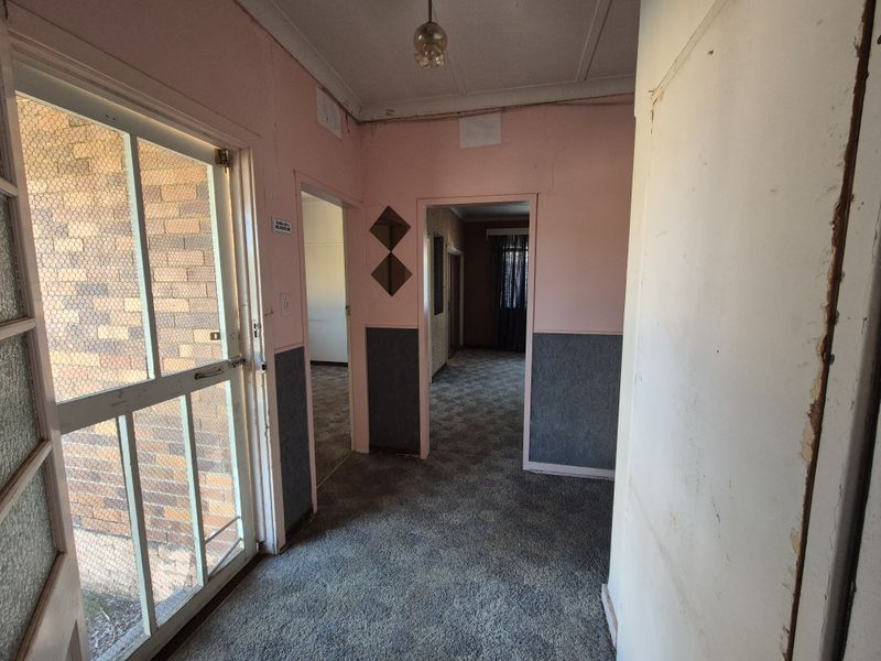 An empty hallway featuring carpeted flooring and access to adjacent rooms, showing signs of wear and requiring cosmetic updates.