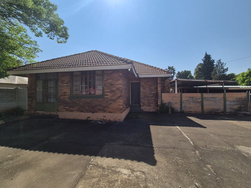 Front view of a single-story brick house featuring a tiled roof, concrete driveway, and an attached carport with a perimeter boundary wall.