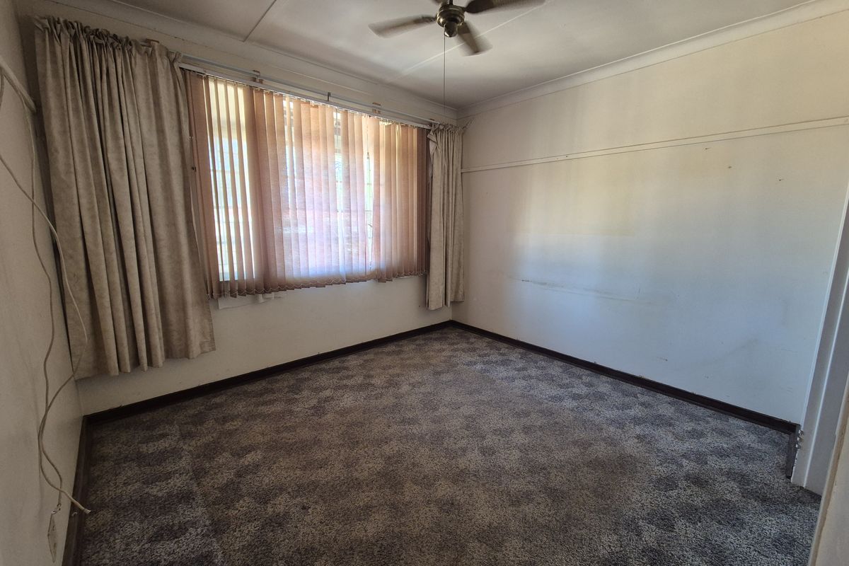 An empty bedroom featuring carpet flooring, a ceiling fan, and large windows with vertical blinds, offering a blank canvas for renovation.