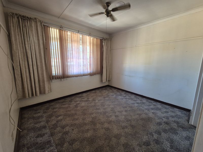 An empty bedroom featuring carpet flooring, a ceiling fan, and large windows with vertical blinds, offering a blank canvas for renovation.