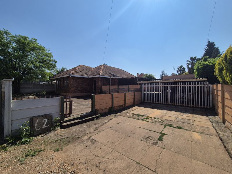 Front exterior view of a single-story brick house featuring a tiled roof, paved driveway, and secure gated carport access.