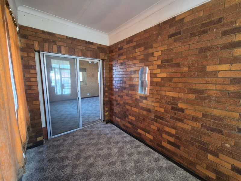 An empty living area featuring exposed brick walls, carpet flooring, and a sliding glass door leading to an adjacent room.