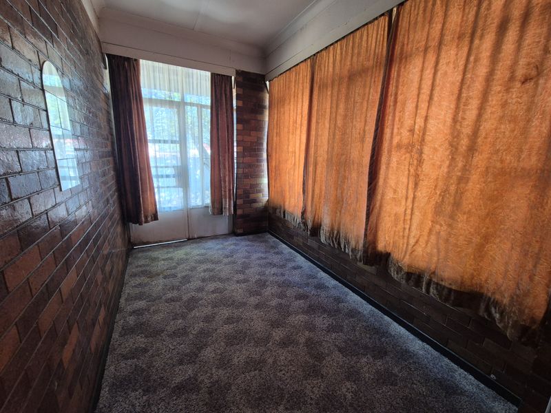 An empty living area featuring exposed brick walls, carpeted flooring, and large windows providing natural light.