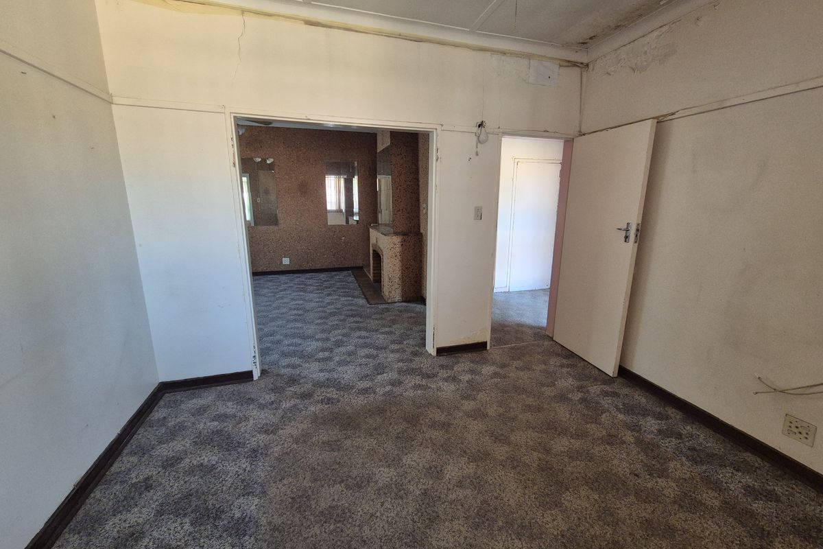 An empty living room featuring a fireplace, carpeted flooring, and visible signs of wear including ceiling water damage and cracked wall plaster.