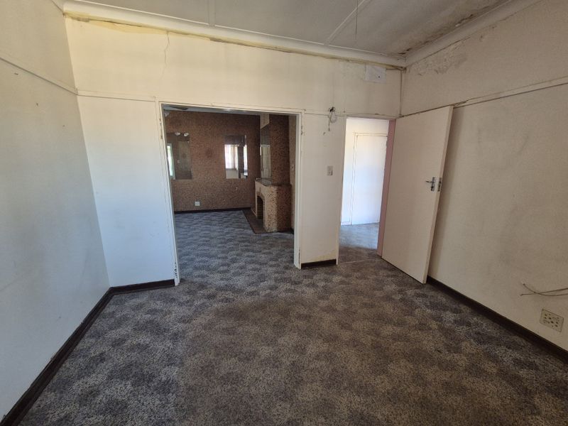 An empty living room featuring a fireplace, carpeted flooring, and visible signs of wear including ceiling water damage and cracked wall plaster.