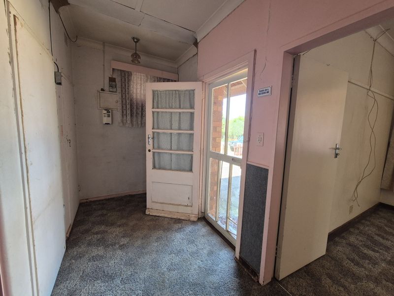 An entry area featuring a timber door, security screen, and carpet flooring, requiring cosmetic updates and repairs to wall finishes and electrical fixtures.