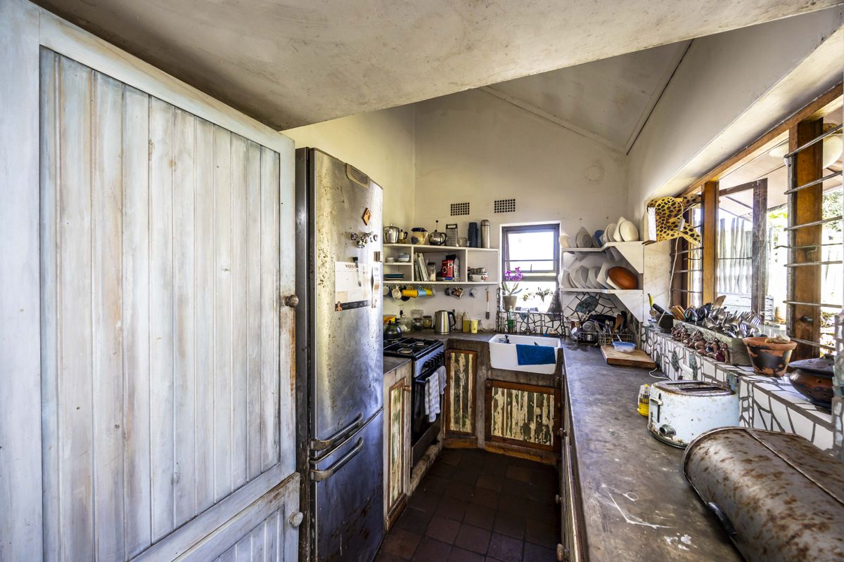 A rustic kitchen featuring a farmhouse sink, gas stove, and open shelving, requiring significant cosmetic updates to modernize the space.